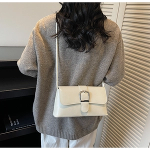 Detail of minimalist beige faux leather shoulder bag with silver buckle worn by a model