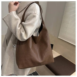 Detail of a deep brown woven hobo bag with intricate leather texture and wide shoulder strap