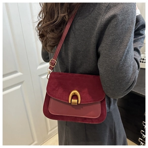 Detail of burgundy flap bag with suede texture and a golden horseshoe metal buckle
