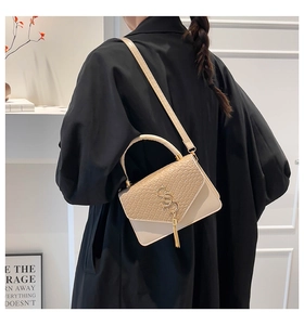 Detail of cream crossbody bag with faux-crocodile texture and gold tassel hanging on a bag