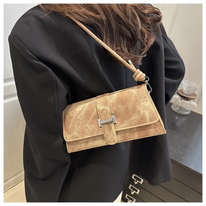 Detalle de bolso bandolera de ante marrón con hebilla metálica plateada en forma de H