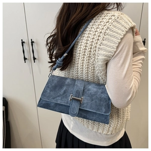 Close-up of blue suede shoulder bag with silver buckle and knotted strap detail