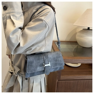 Detail of grey suede shoulder bag with silver H-buckle on a minimalist beige trench coat