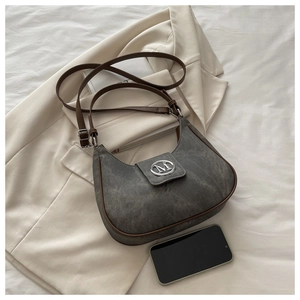 Détail du sac demi-lune gris foncé avec logo M argenté sur fond de blazer beige classique