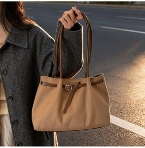 Detail of camel tote bag with dark brown leather handles and silver buckle in sunset light