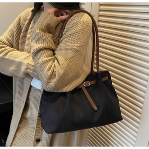 Detail shot of black tote bag with brown leather straps worn by model in knit cardigan