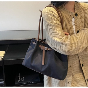 Detail showing high-quality navy canvas tote with brown leather handles and buckle strap