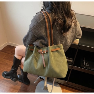 Olive green canvas tote bag with brown leather straps shown on shoulder for daily commute