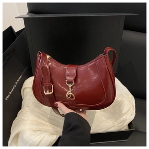 Gros plan d'un sac selle en cuir verni bordeaux dans son coffret avec fermoir doré
