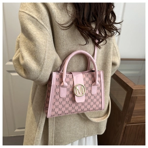 Detail view of pink leather handbag with golden M buckle and patterned shoulder strap