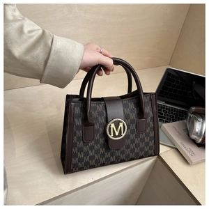 Classic brown shoulder bag with M-letter print and gold metal buckle on wooden stairs