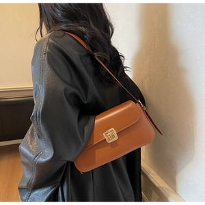 Sac sous le bras en cuir mat marron avec fermoir doré porté sur une veste en cuir noir