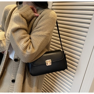 Détail d'un sac sous le bras noir minimaliste avec fermoir doré sur une tenue beige
