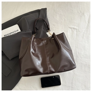 Detail of dark brown glossy leather tote bag with gold hardware and wrinkled texture