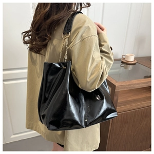 Detail of black glossy tote bag with golden chain strap on model in a home setting