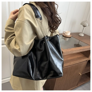 Detail of black patent leather tote bag with gold chain strap in a cozy home setting