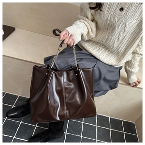Detail of dark brown leather tote bag with metallic chain straps on a wooden background