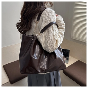 Detail of glossy deep brown tote bag featuring fine stitching and gold chain accents