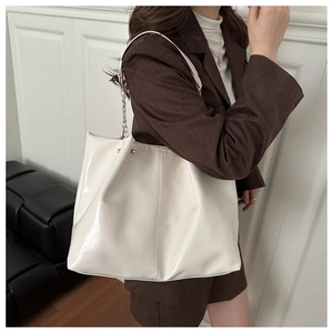 Detail of a large cream tote bag with glossy finish and metal chain strap on model
