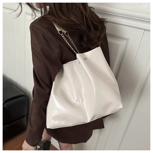 Close-up of cream glossy tote bag with gold chain strap on shoulder of a brown suit