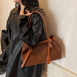 Retro leopard print tote bag with brown leather straps shown on shoulder with black coat