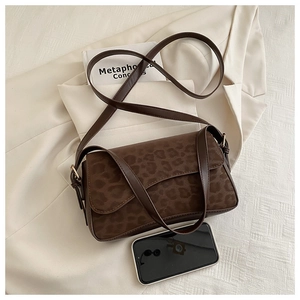 Detail view of leopard print shoulder bag with adjustable strap beside a smartphone