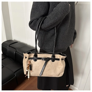 Detail of beige suede tote bag with black leather accents and beaded pendant accessory