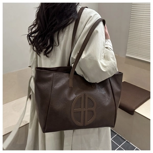 Detail of dark brown leather tote bag with embossed round logo and litchi grain texture