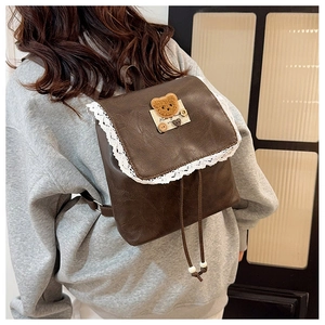 Dettaglio zaino in pelle marrone con bordo in pizzo e stemma dell'orso sul davanti