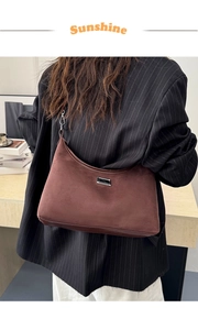 Détail du sac demi-lune en daim marron foncé avec plaque métallique argentée porté à l'épaule