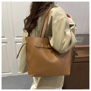 Detail of tan leather tote bag with decorative buckle strap worn with khaki trench coat