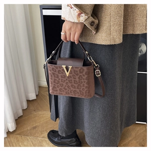 Detailed view of leopard print handbag featuring a gold V-shaped buckle and brown leather flap