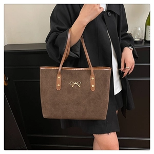 Close-up of brown suede tote bag with golden bow ornament and rivet details on the handle