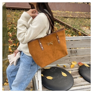 Brown suede tote bag with golden bow detail shown in a cozy outdoor autumn park setting