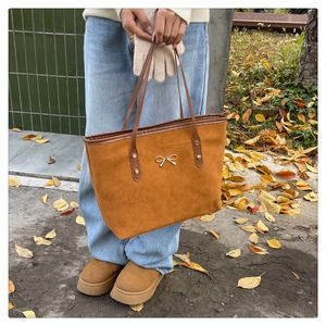 Brown suede tote bag with gold bow detail paired with casual winter outfit and leaves