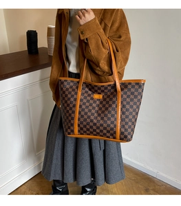 Detail of checkered tote bag showing brown leather straps and large capacity styling