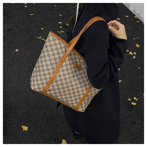 Detail of monogram tote bag with brown leather straps held against autumn leaves