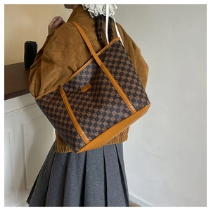 Detail of a large printed tote bag with a brown checkered pattern shown on a shoulder