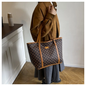 Detail of checkered tote bag with leather handles shown on shoulder with suede jacket