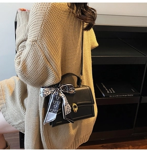 Close-up of black leather crossbody bag with gold lock and bear print silk scarf