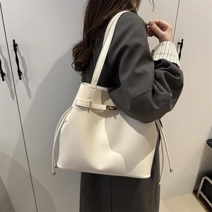 Cream white faux leather tote bag with gold clasp shown on a model in a minimal interior