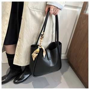 Detail of black faux leather tote bag with elegant silk scarf on handle and snap closure