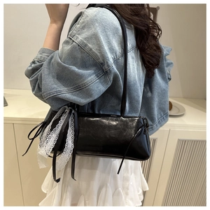 Detail of black leather underarm bag featuring delicate white lace bow and silk ribbons