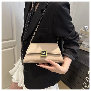 Detail of beige crossbody bag with gold M-buckle and chain strap on a black suit jacket