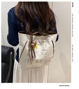 Detailed back view of a white canvas tote bag with brown leather trim and bear charm