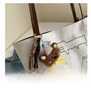 Close-up of a plush bear keychain with polka dot hat on a canvas tote bag accessory