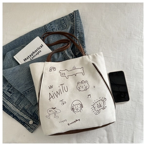 Detailed view of white canvas tote bag with brown leather straps and cartoon illustrations