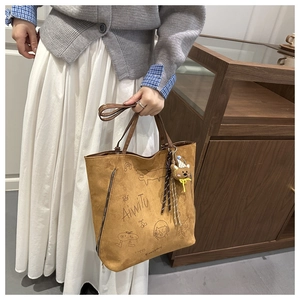 Detailed view of brown matte tote bag with artistic graffiti prints and bear pendant