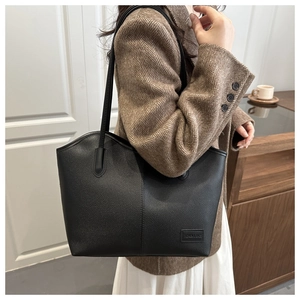 Black litchi grain leather tote bag worn by a model in a stylish brown blazer jacket