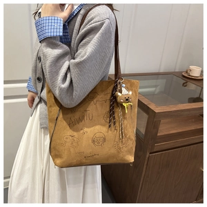 Brown suede tote bag with cartoon print and bear charm shown in a cozy indoor setting